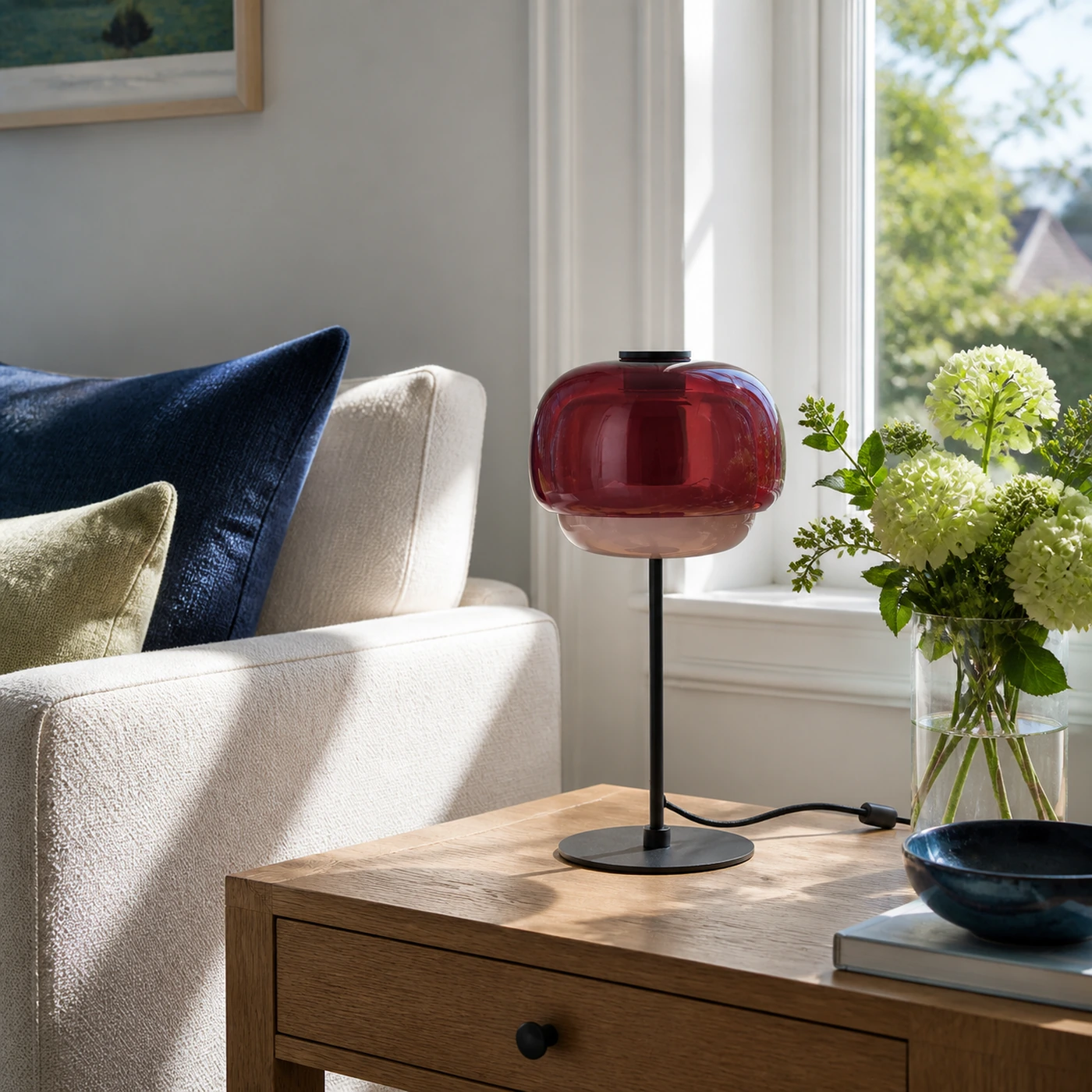 Burgunderrote Ava-Lampe auf einem sonnenbeschienenen Beistelltisch im Wohnzimmer