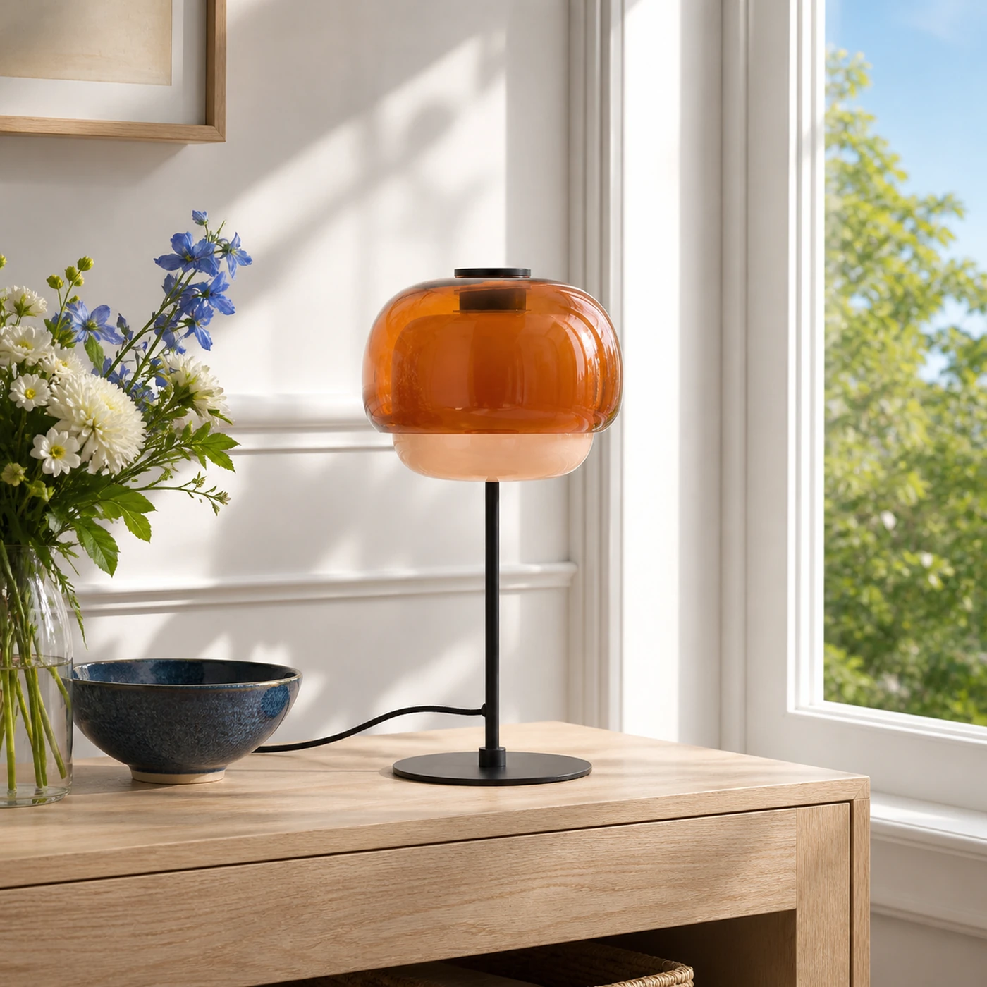 Orangefarbene Ava-Tischleuchte aus doppelwandigem Glas auf einer sonnenbeschienenen Eingangskonsole